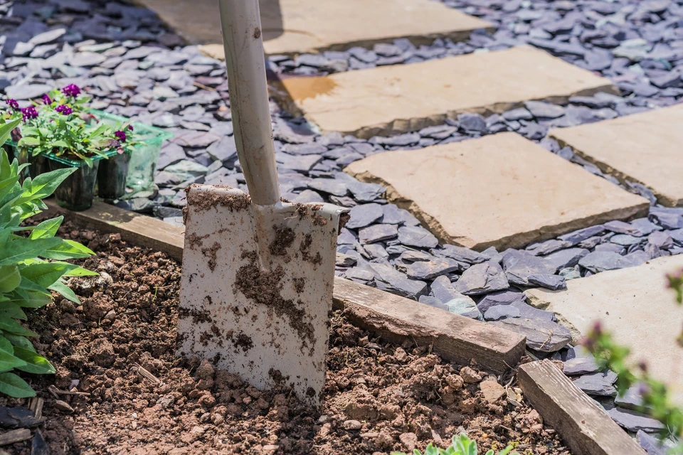 Scène extérieure de jardinage avec bêche plantée dans terre cultivée près d'un carré potager en bois