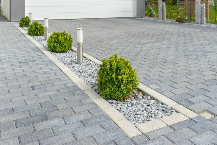 Allée de jardin pavée en briques avec motif en chevrons, bordée de pelouse verte et plantations paysagères variées