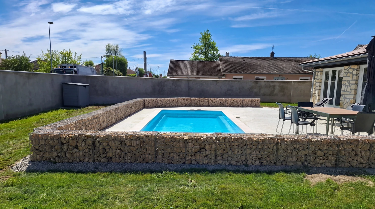 Piscine rectangulaire &agrave; coque polyester bleue, semi-enterr&eacute;e, sur&eacute;lev&eacute;e sur une plateforme en b&eacute;ton cir&eacute;