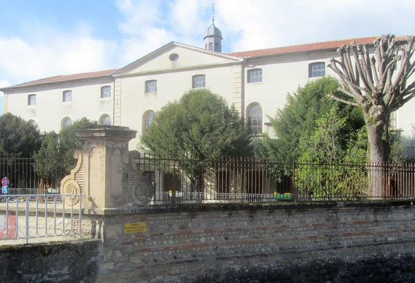 Vue de rue typique de Montluel avec des maisons r&eacute;sidentielles, des petits immeubles locaux et commerces, une rue calme avec trottoirs, montrant l'environnement urbain et p&eacute;riurbain o&ugrave; intervient le paysagiste. Le style architectural doit &ecirc;tre caract&eacute;ristique d'une commune de l'Ain (Rh&ocirc;ne-Alpes), avec un ciel d&eacute;gag&eacute; et une ambiance diurne claire. L'image doit transmettre une impression de proximit&eacute; et d'accessibilit&eacute; locale.