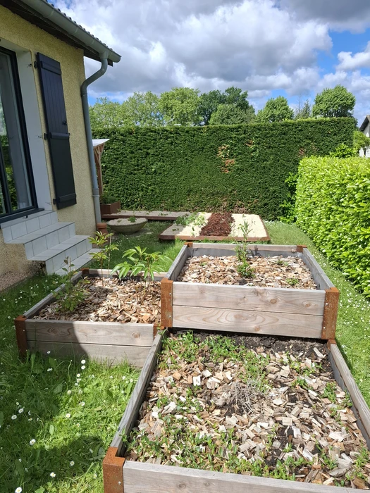 Jardin partagé urbain ensoleillé avec potager surélevé en acier galvanisé anthracite à parois ondulées, pergola en bois douglas, carrés potagers en béton préfabriqué, abri de jardin en métal, arrosoir, récupérateur d'eau